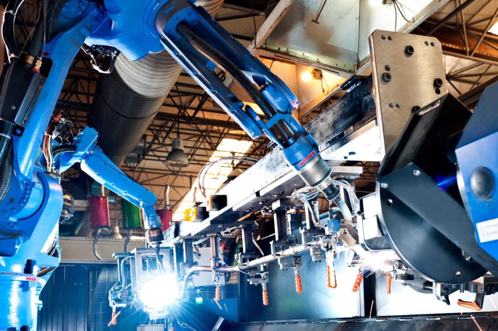 Robotic arms working on an assembly line in a factory setting, with bright lights illuminating the machinery.