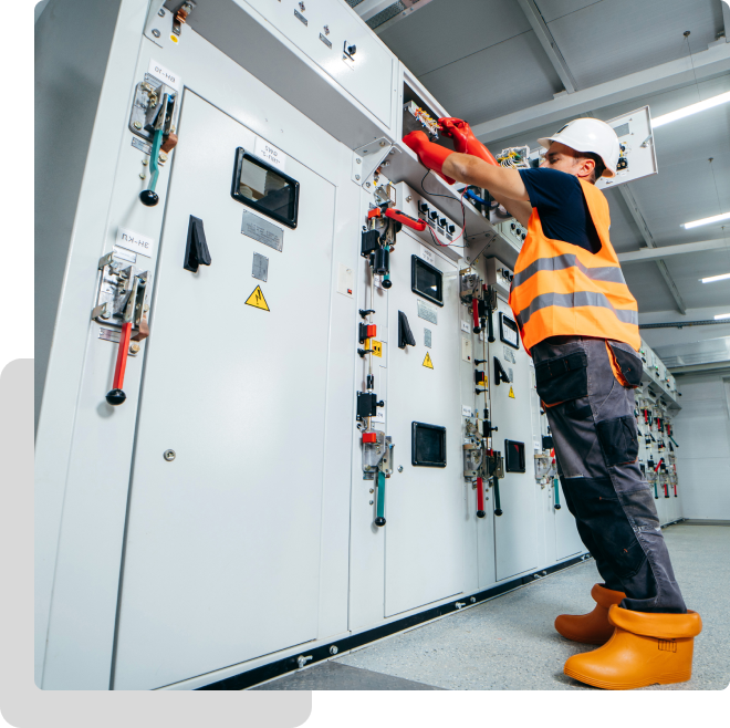 Worker in safety gear operates electrical panel in industrial setting.