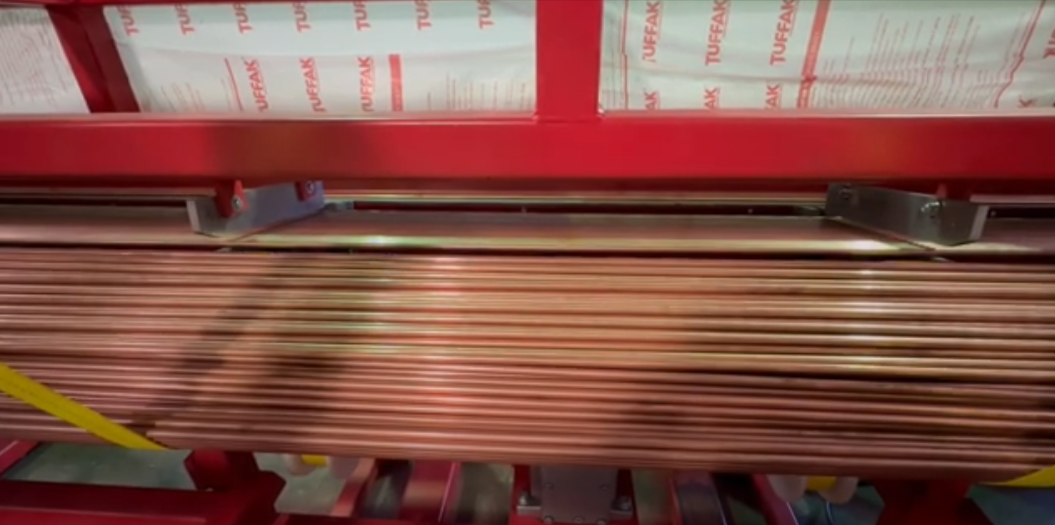 Stacks of copper tubing are arranged on a red industrial rack, with packaged insulation material visible in the background.